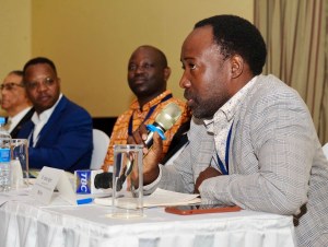 A man speaking into a microphone while others listen attentively.
