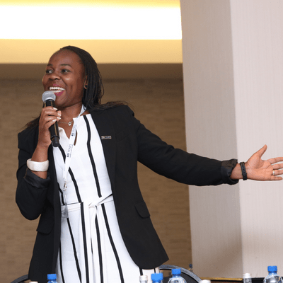 A cheerful woman addressing the audience through a microphone.