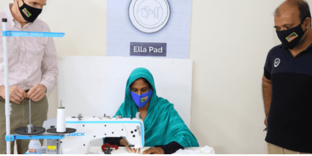 Two men watching a woman work on a sewing machine.