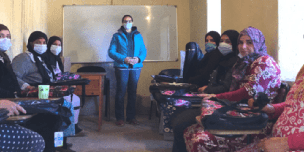 Mina Lalaoui Kamal is positioned in front of a whiteboard, while other women are seated nearby.